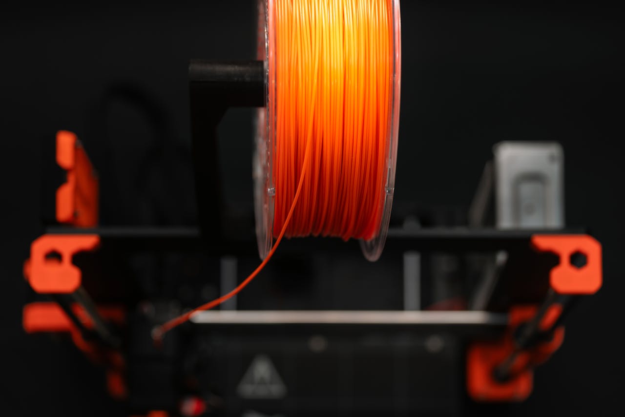 services-06 Close-up of an orange 3D printer filament spool in a workshop setting, highlighting innovation and design.
